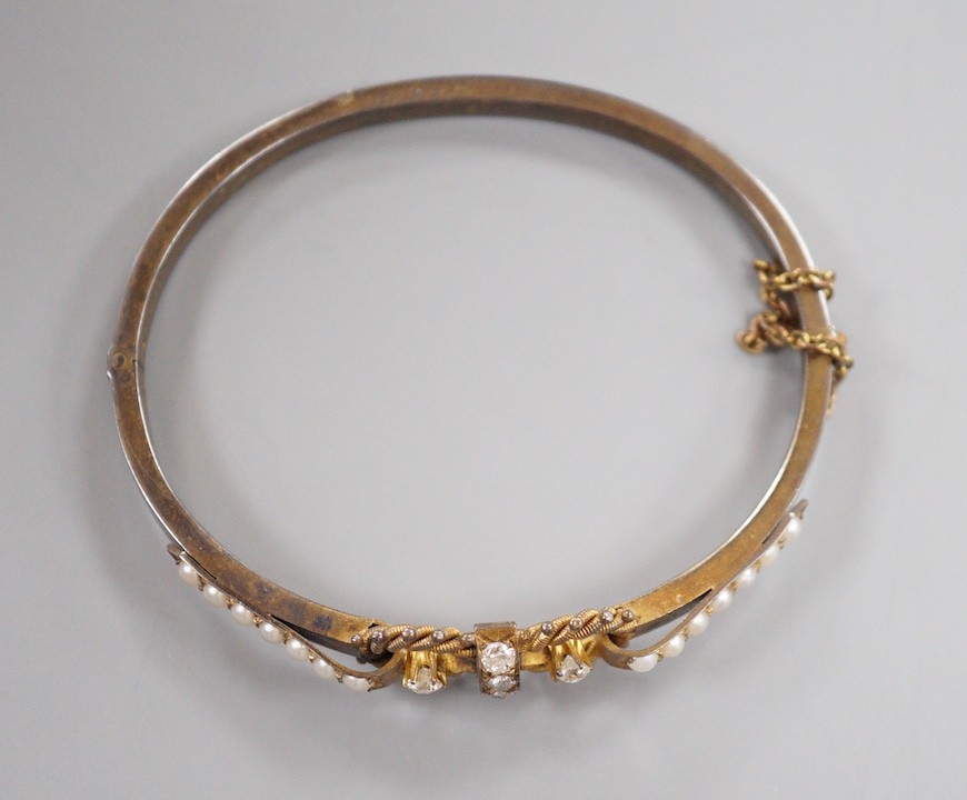 A late Victorian yellow metal, six stone diamond cluster set hinged bangle, with split pearl set shoulders, interior diameter 56mm, gross weight 10.5 grams.